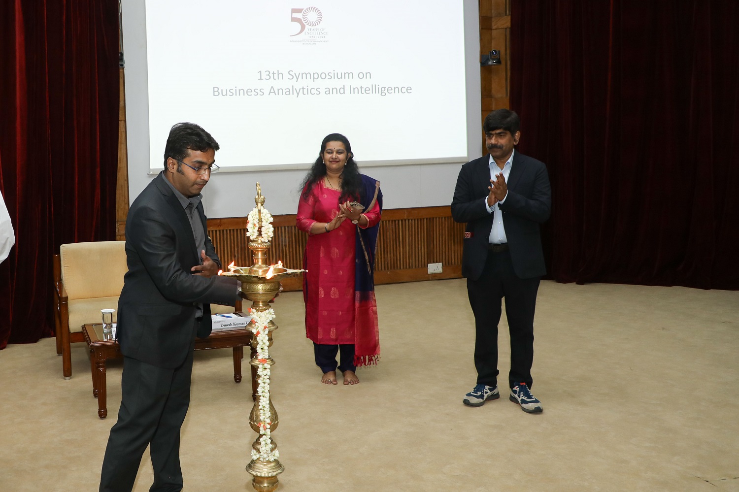 A participant lights the lamp to inaugurate the 13th Symposium on Business Analytics & Intelligence on 21st July 2023. Prof. U Dinesh Kumar, Chairperson, Data Centre and Analytics Lab, IIMB, looks on.
